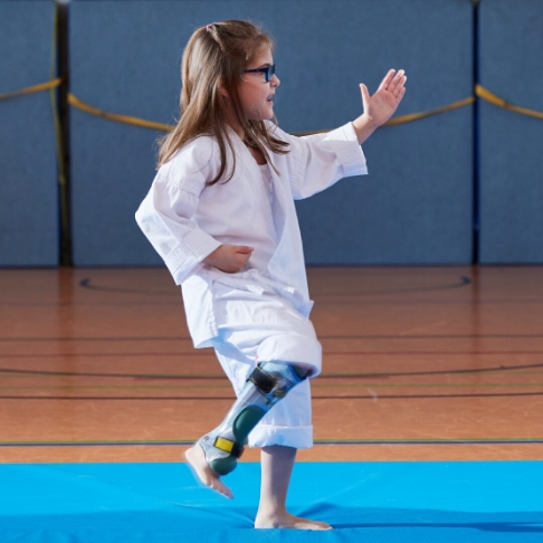 Mädchen mit Unterschenkelorthesen in Karate-Position in der Turnhalle