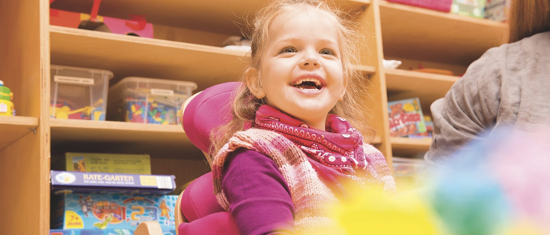 Lachendes Mädchen sitzt in einem Therapiestuhl im Kindergarten