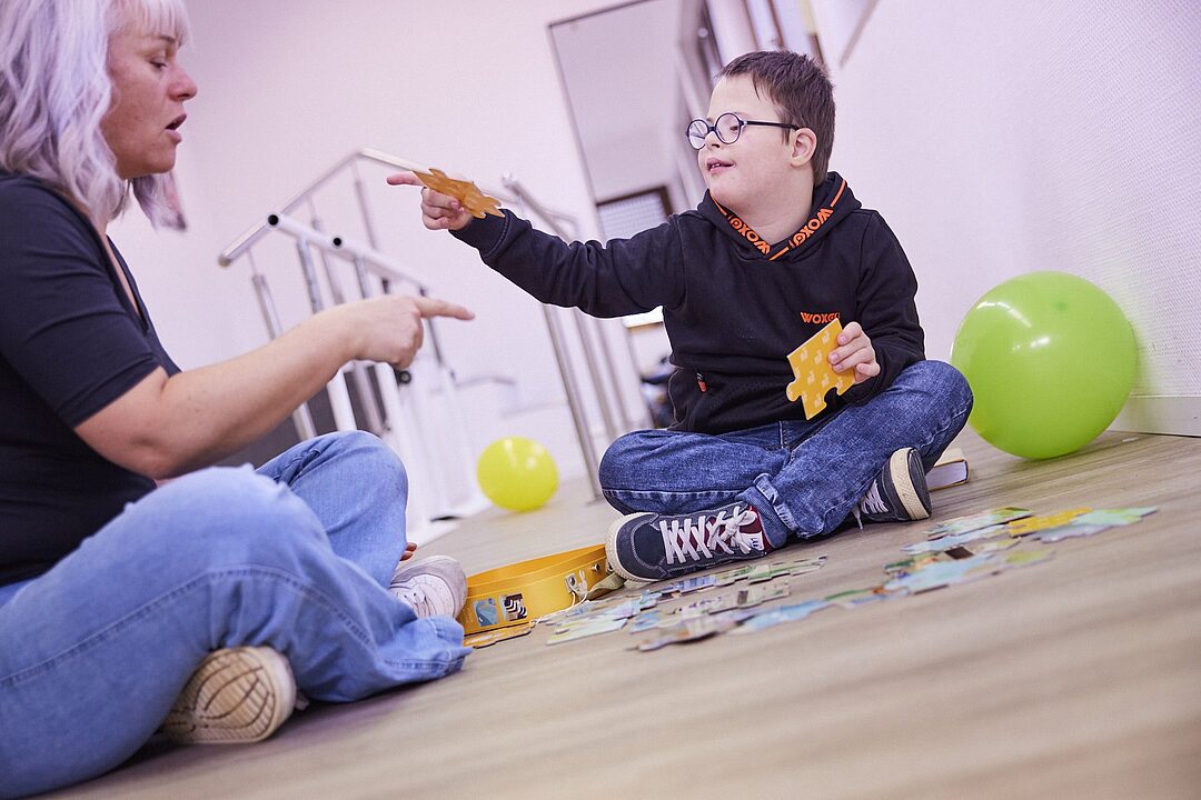 Therapeutin legt mit einem Jungen ein Puzzle auf dem Boden