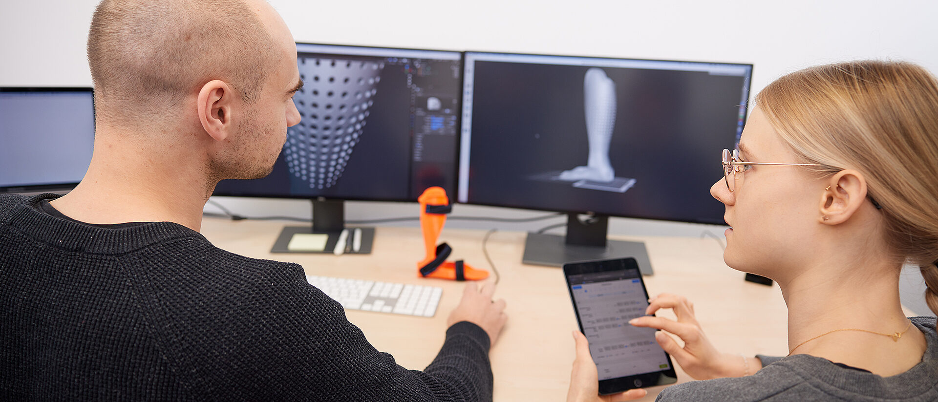 Zwei Mitarbeitende konstruieren eine Orthese am Computer