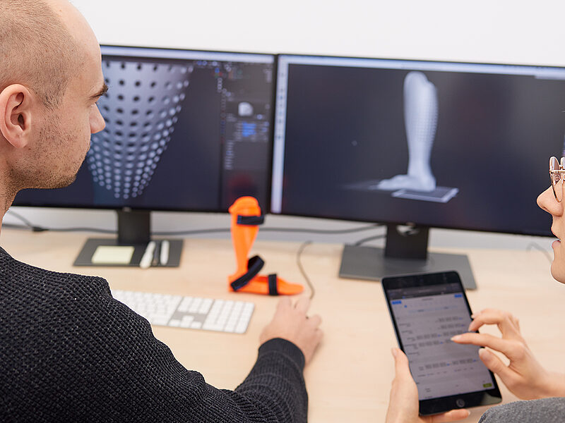 Zwei Mitarbeitende konstruieren eine Orthese am Computer