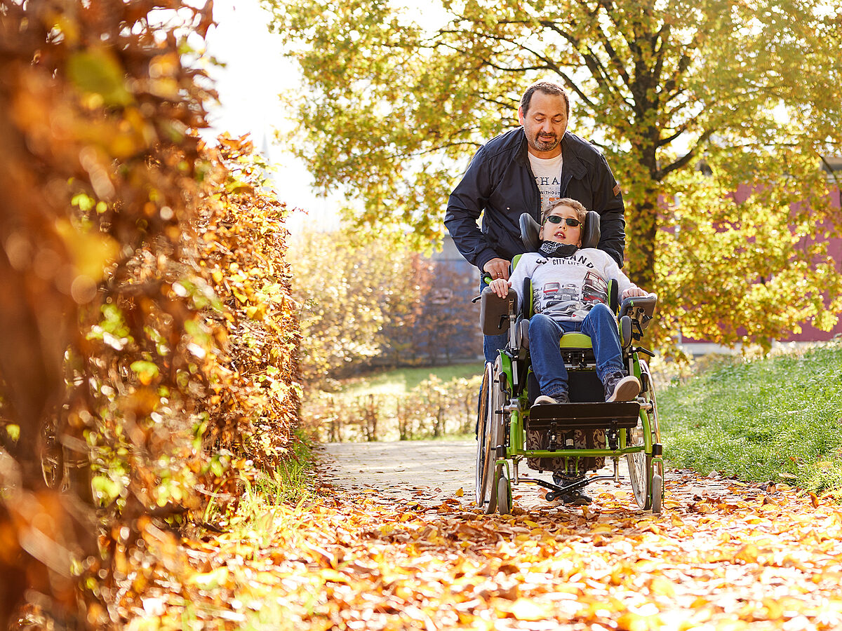 Mann mit Kind im Reha-Buggy im Herbstwald