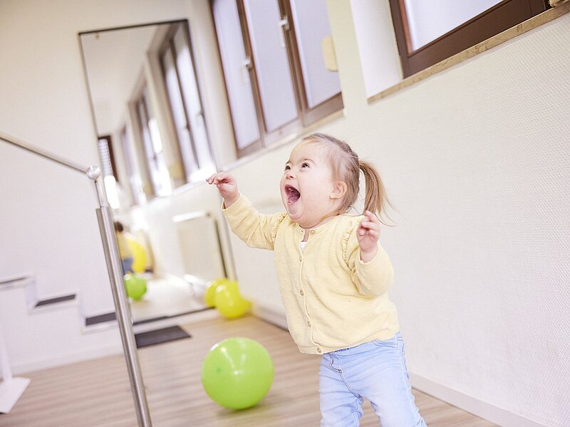 Kleines Mädchen übt das Gehen am Barren im Therapieraum