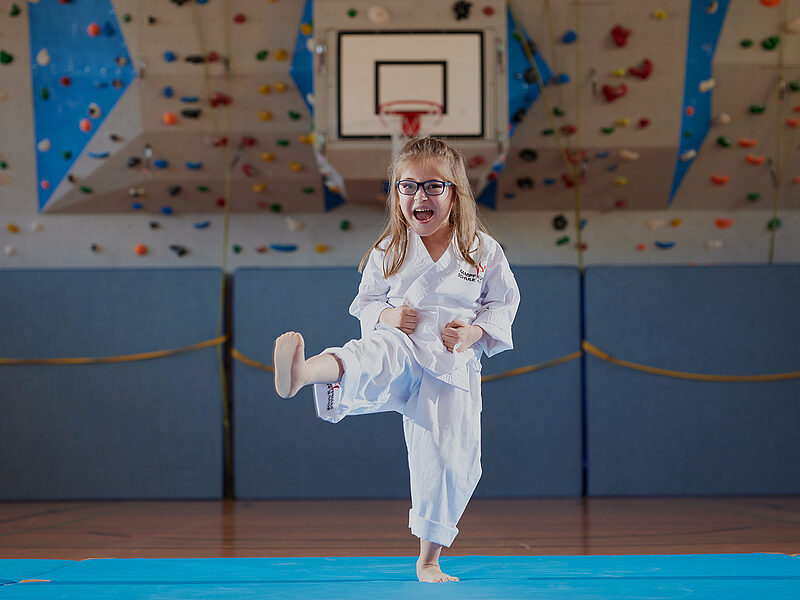 Myriam in Karate-Kleidung macht mit ihrer Beinprothese einen Kick in der Turnhalle