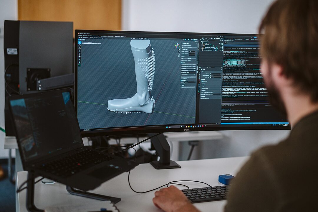 Entwickler arbeitet an der ORFO-Konstruktionssoftware mit dem 3D-Modell einer Orthese und Programmcode