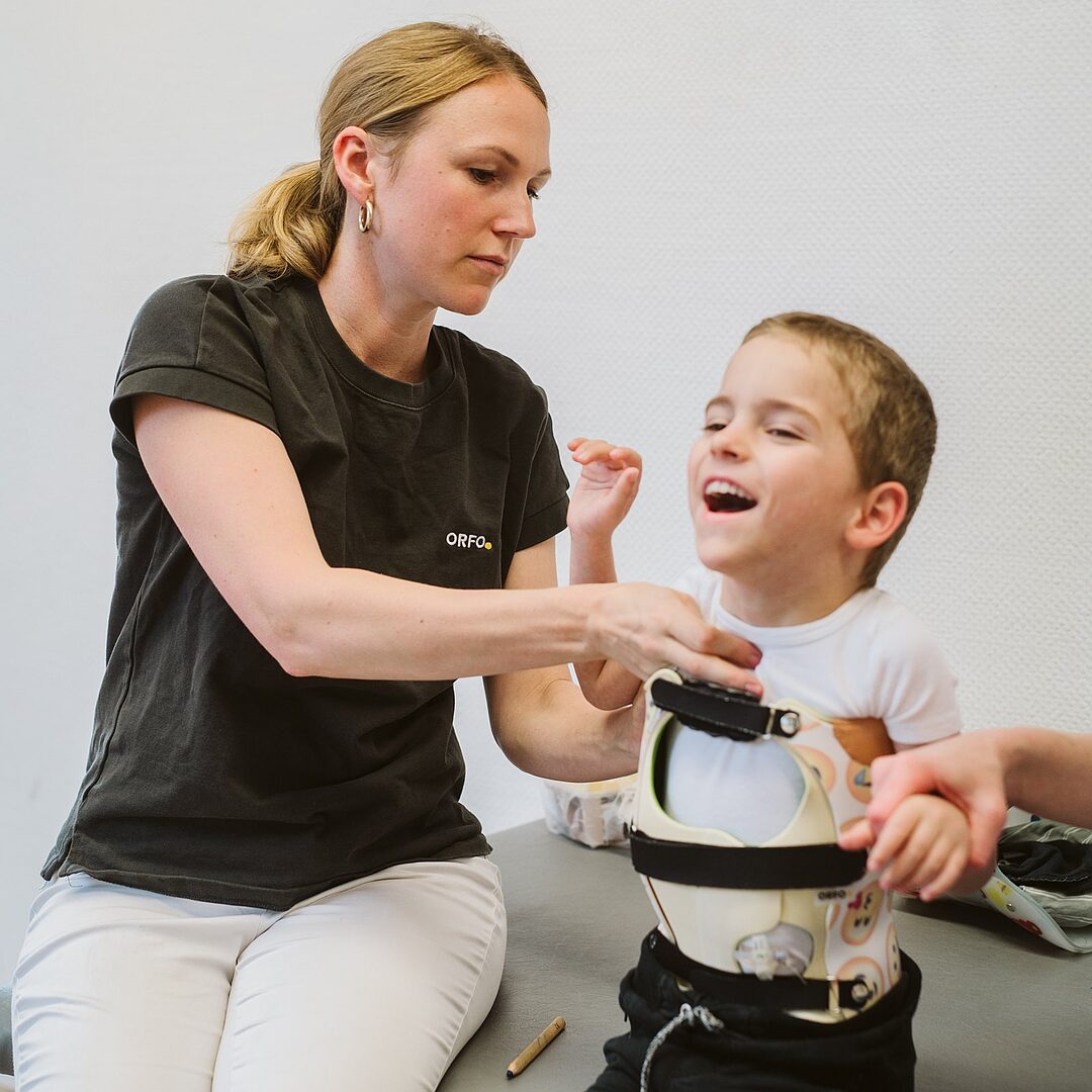 Lachendes Kind bei der Anprobe einer Rumpforthese mit Orthopädietechnikerin