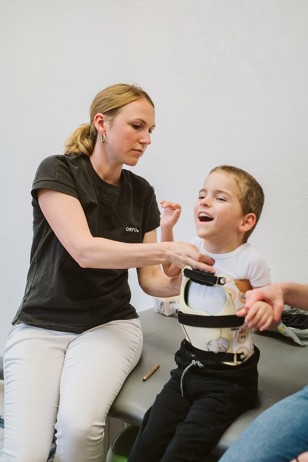 Therapeutin passt einem lachenden Jungen eine Rumpforthese an